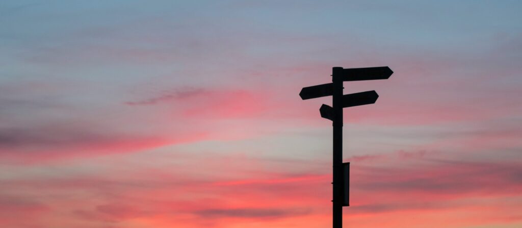 A view of the sunset in the sky with purple and pink clouds behind a signpost indicating brand refresh direction
